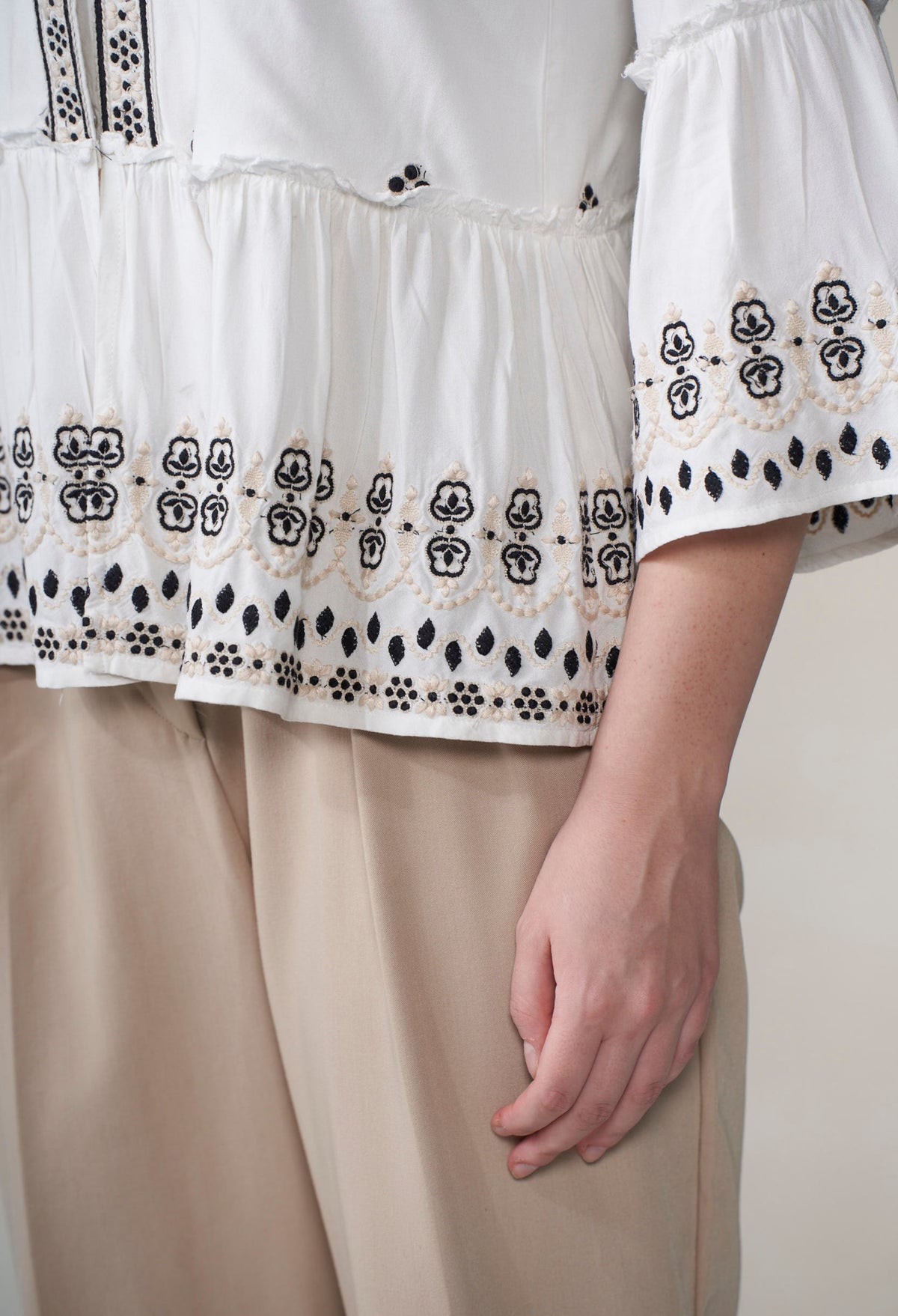 White blouse with black and gold embroidery on a plain background
