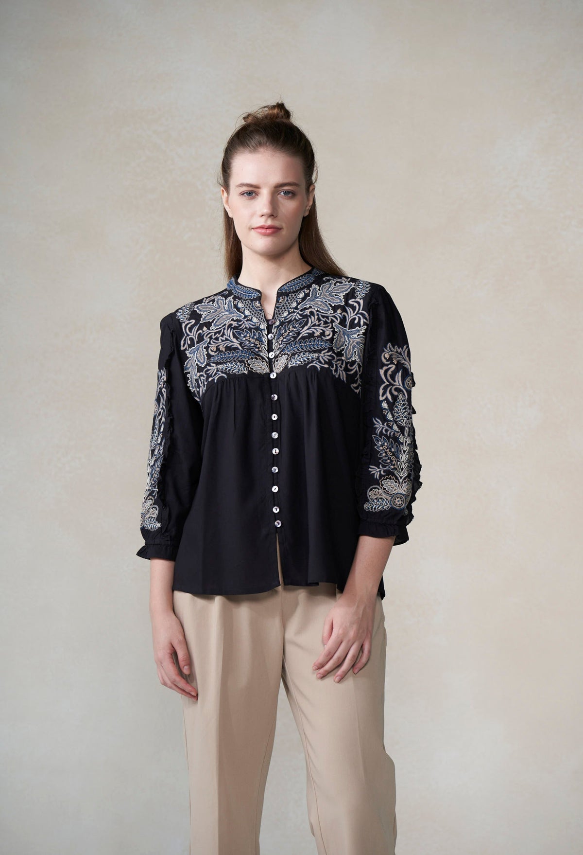 Woman wearing a black blouse with intricate white patterns on a plain background