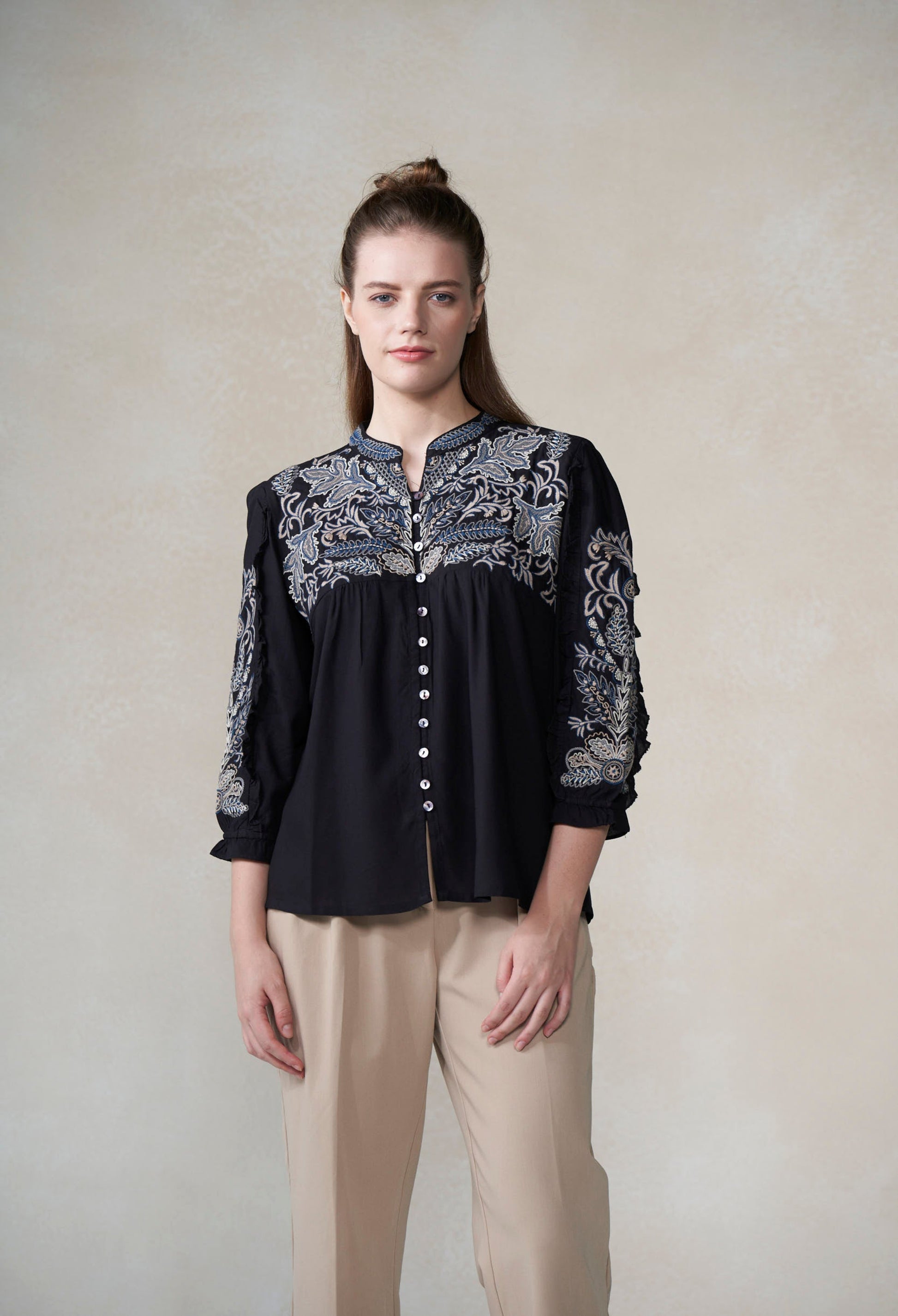 Woman wearing a black blouse with intricate white patterns on a plain background