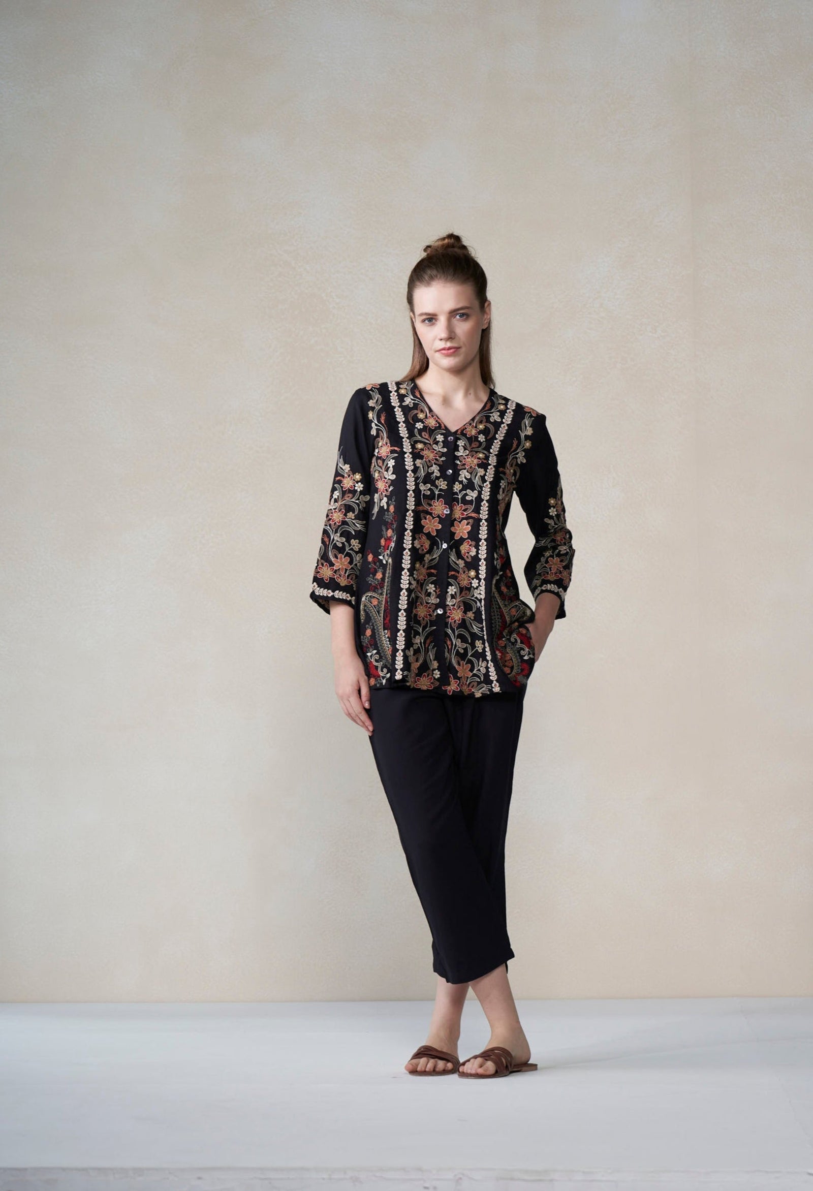 Woman wearing a patterned blouse and black pants against a plain background