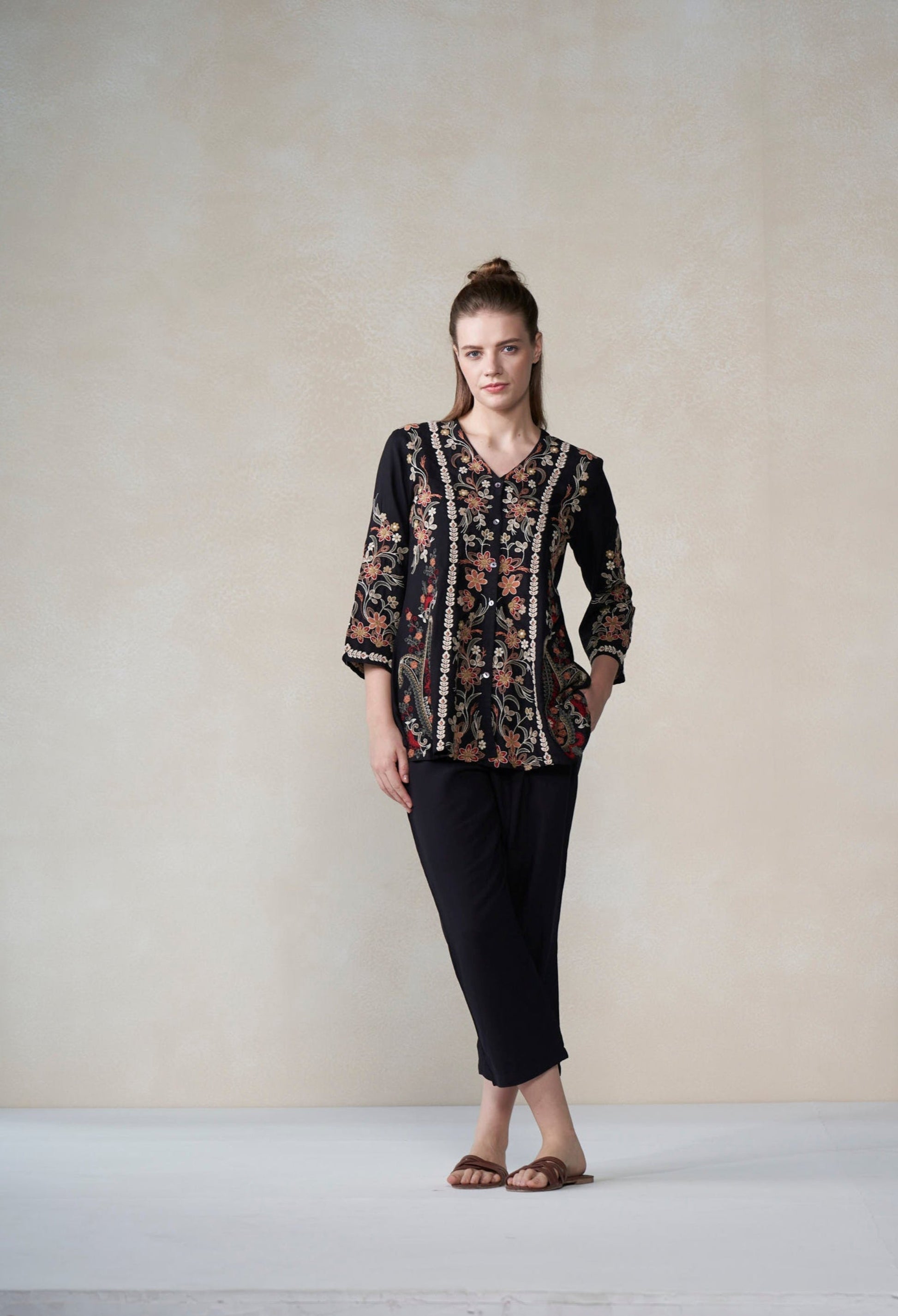 Woman wearing a patterned blouse and black pants against a plain background