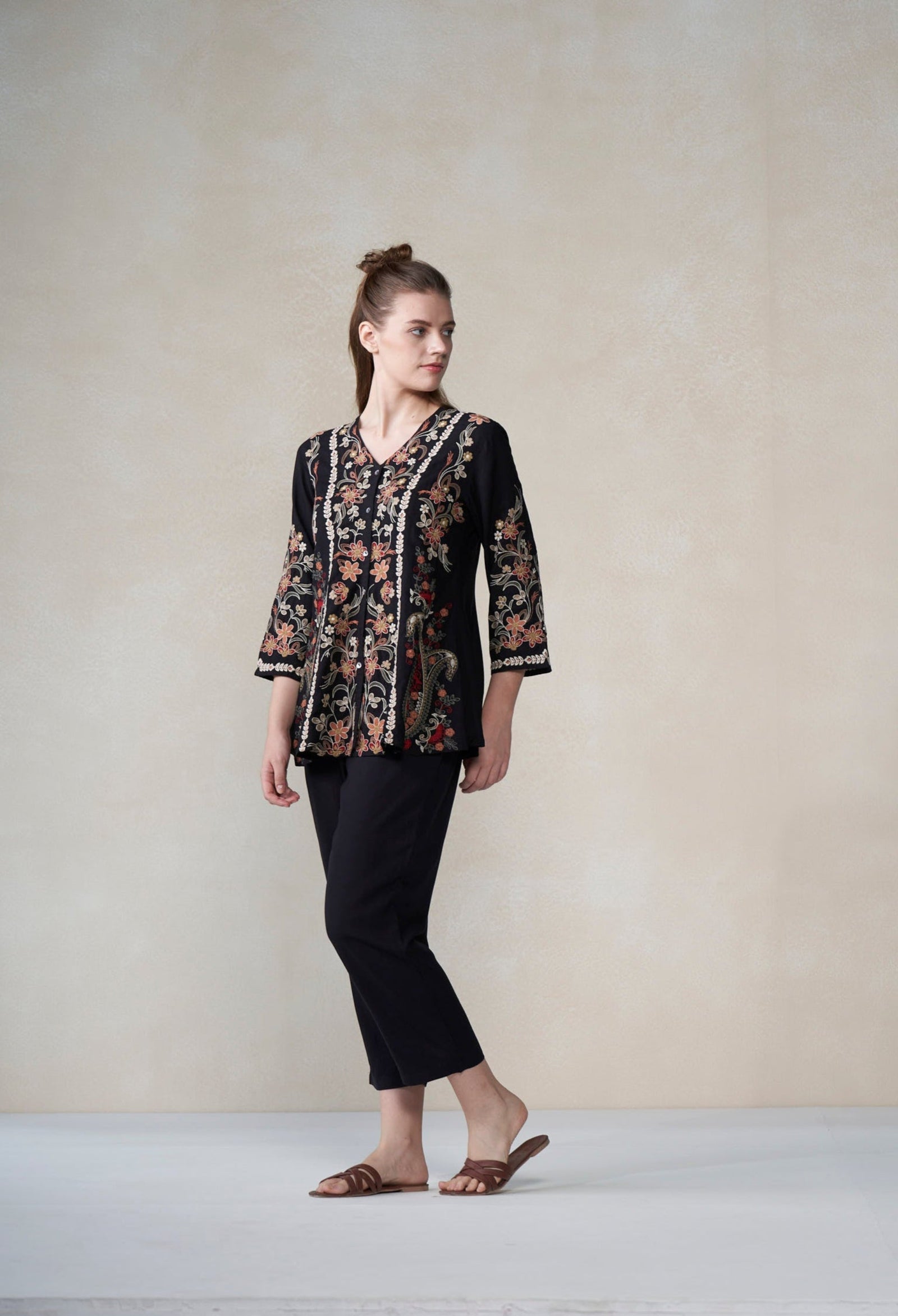 Woman wearing a black floral blouse and black pants against a plain background