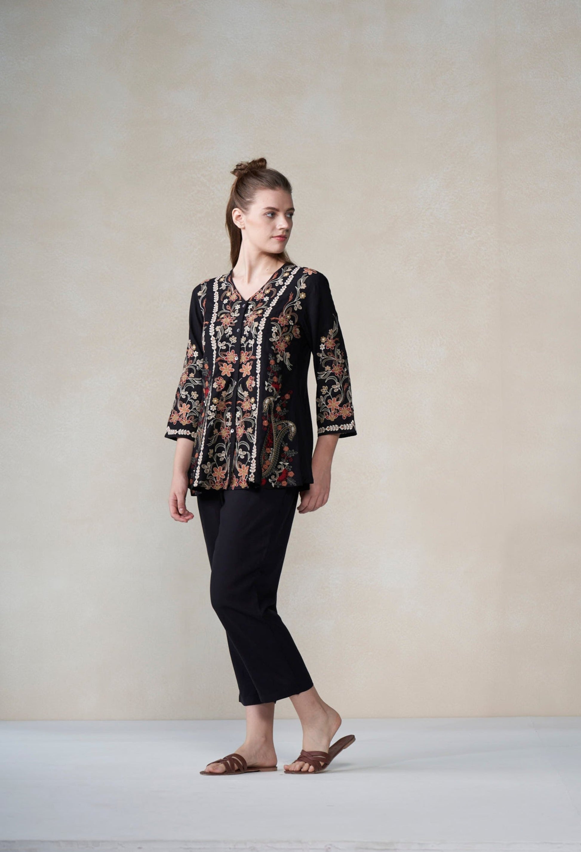 Woman wearing a black floral blouse and black pants against a plain background