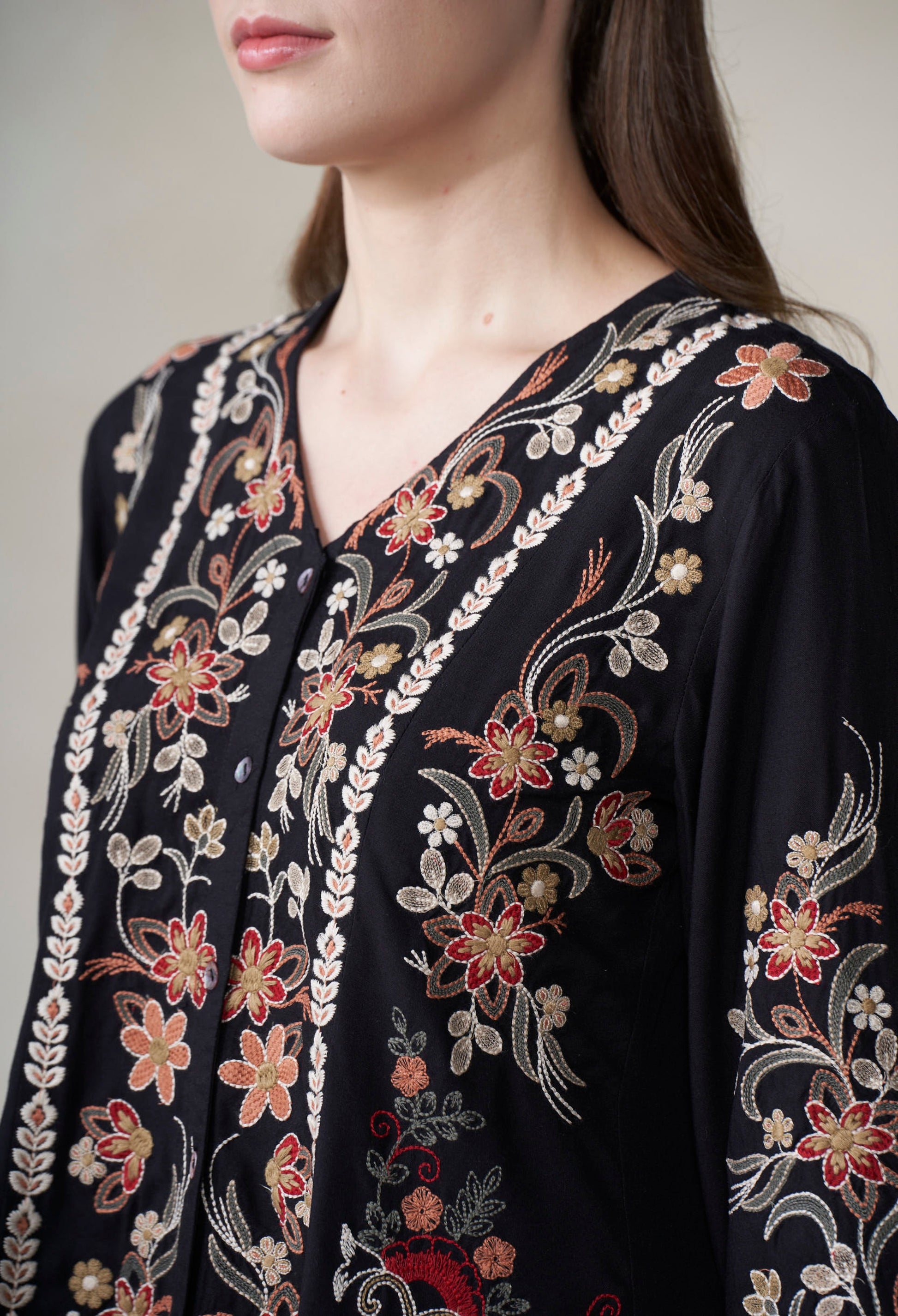 Black embroidered garment with floral patterns on a neutral background