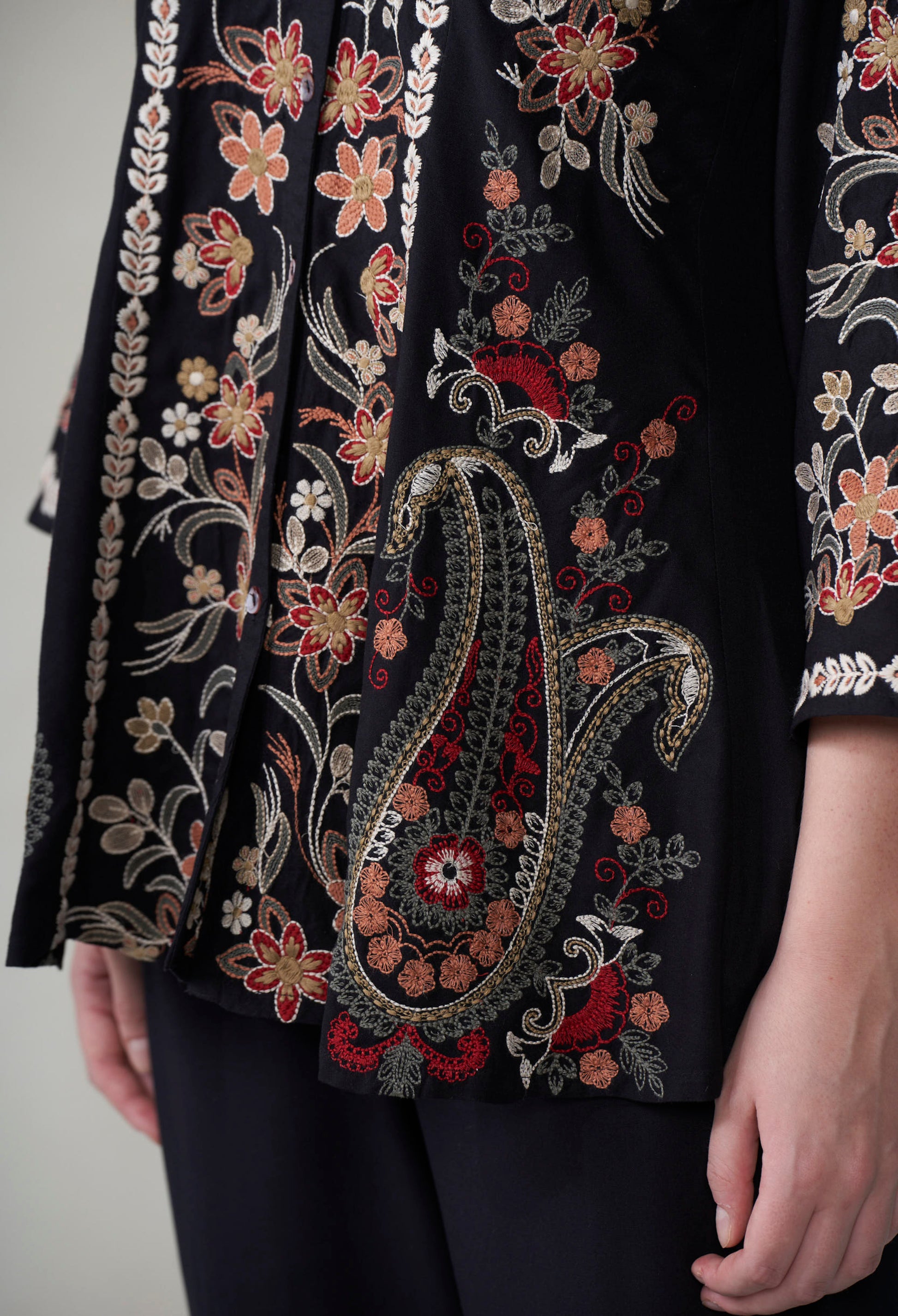 Close-up of a black garment with intricate floral and paisley embroidery.