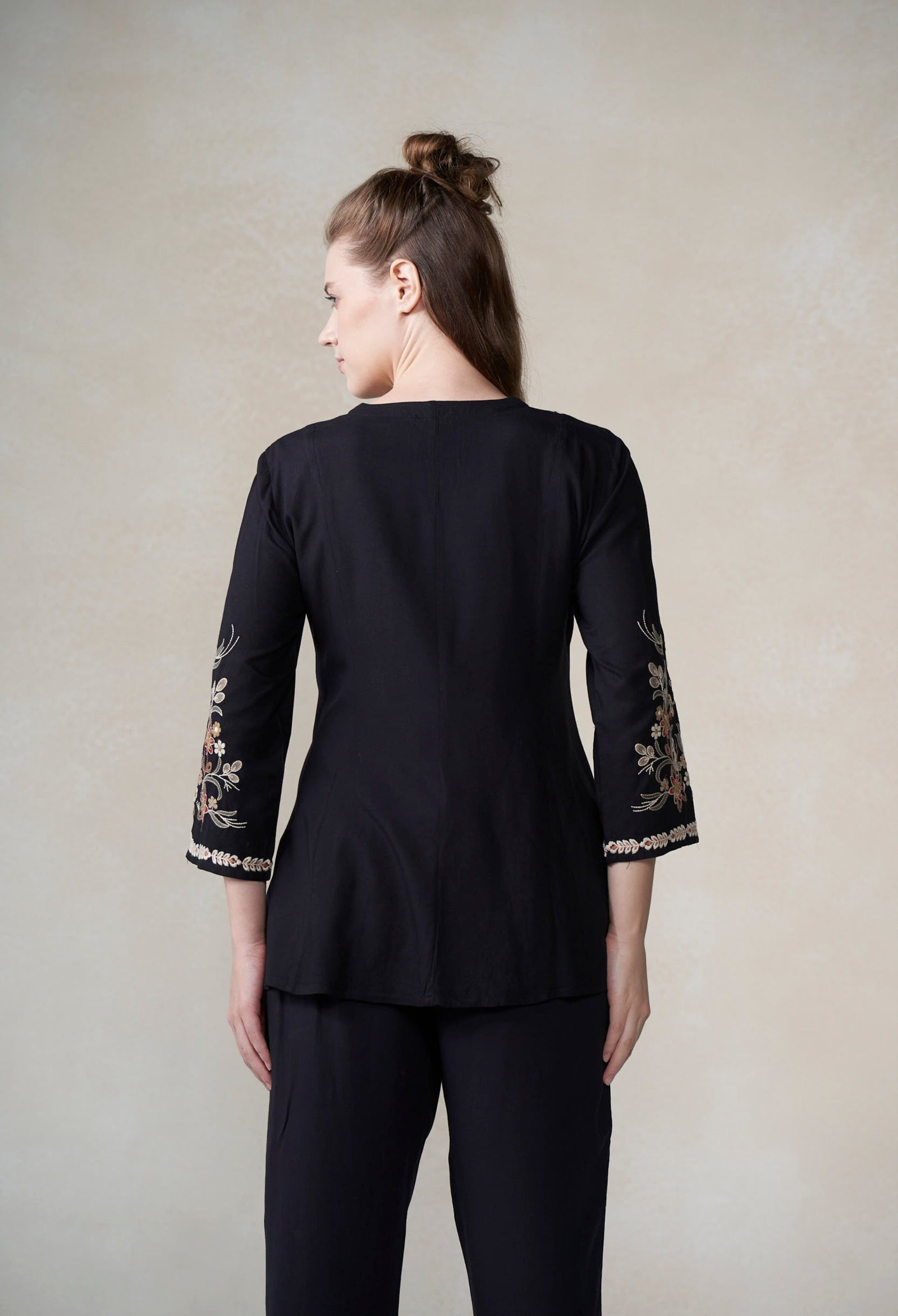 Woman wearing a black outfit with floral embroidery on sleeves against a plain background