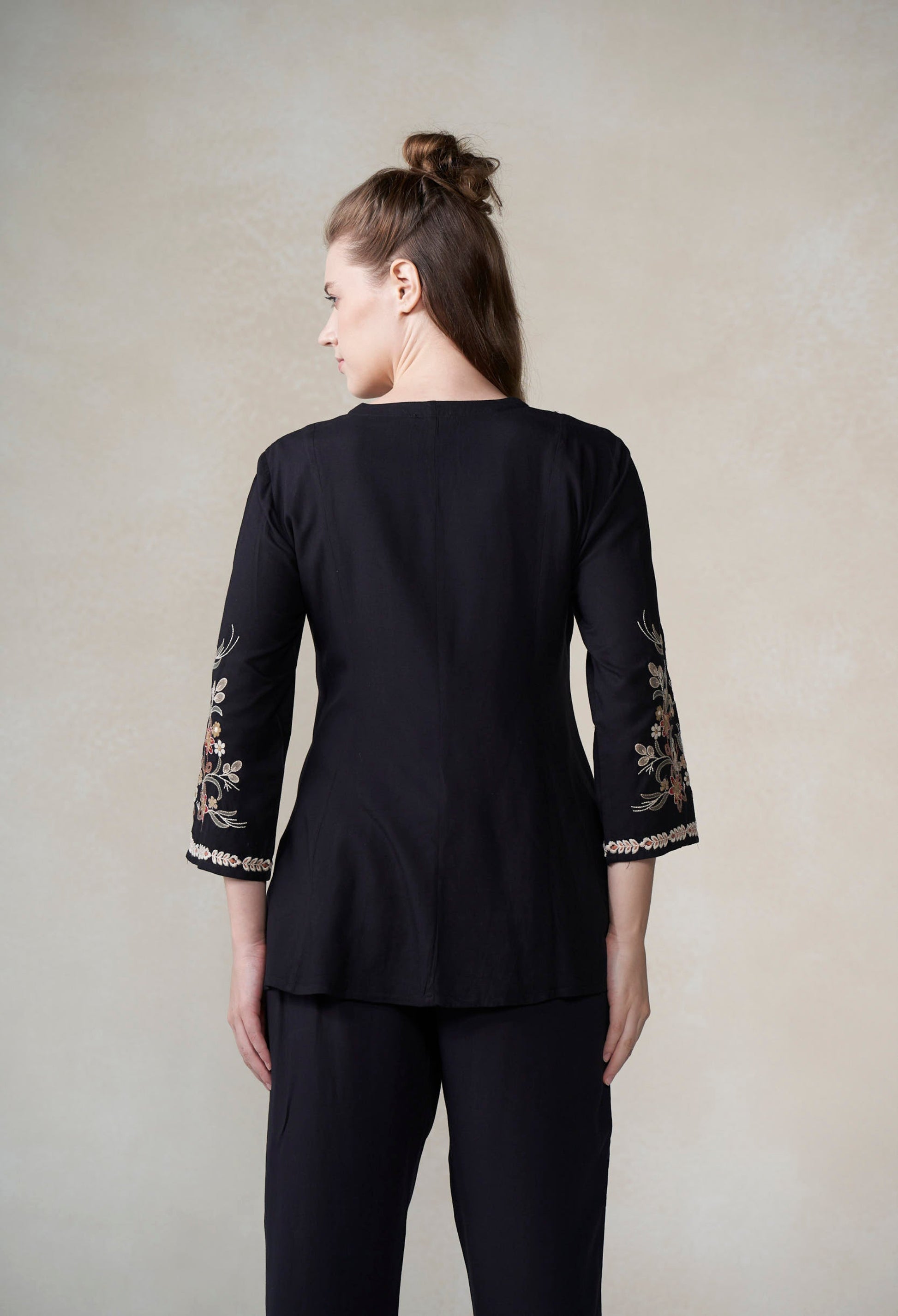 Woman wearing a black outfit with floral embroidery on sleeves against a plain background