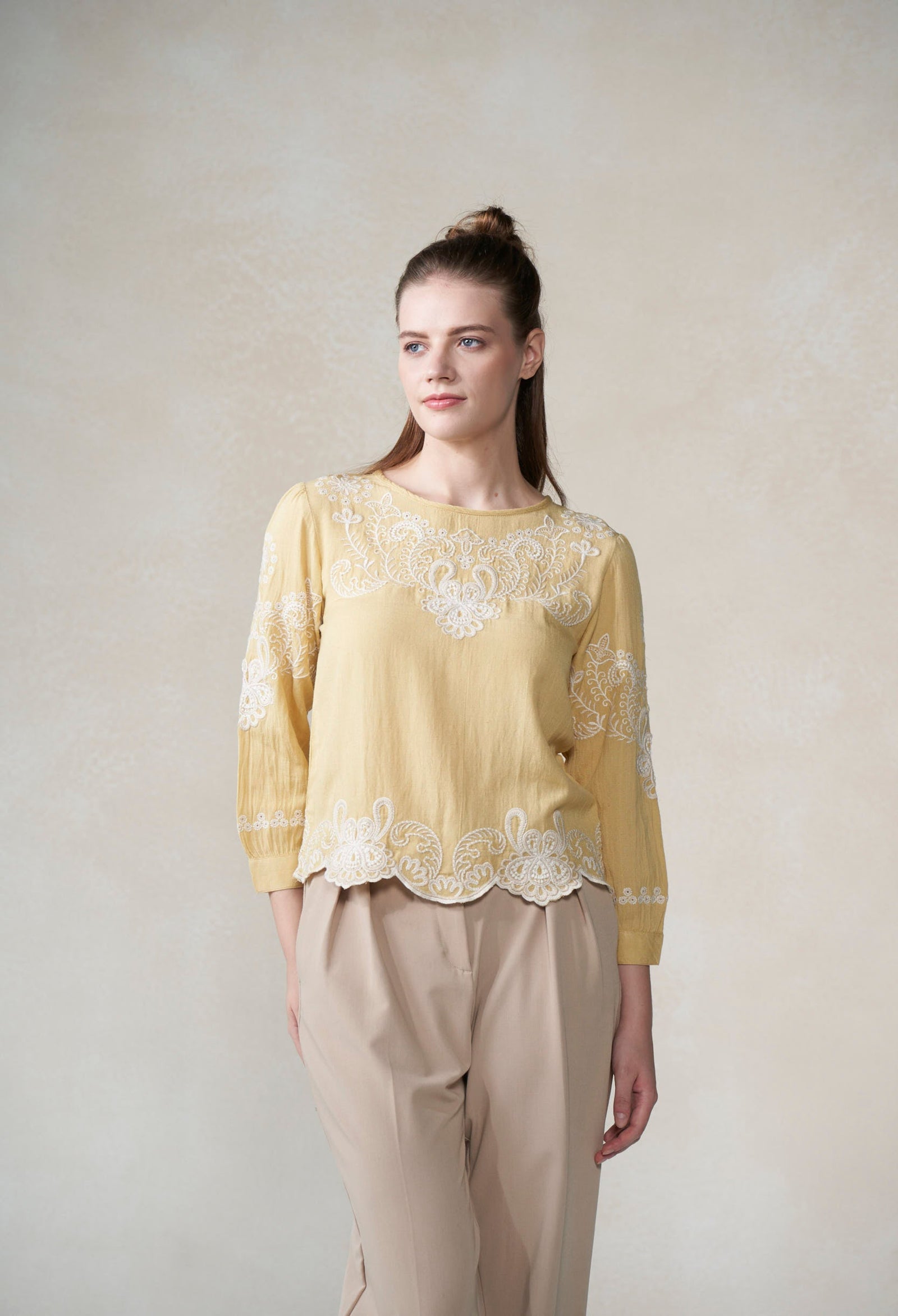 Woman wearing a yellow lace top and beige pants against a plain background