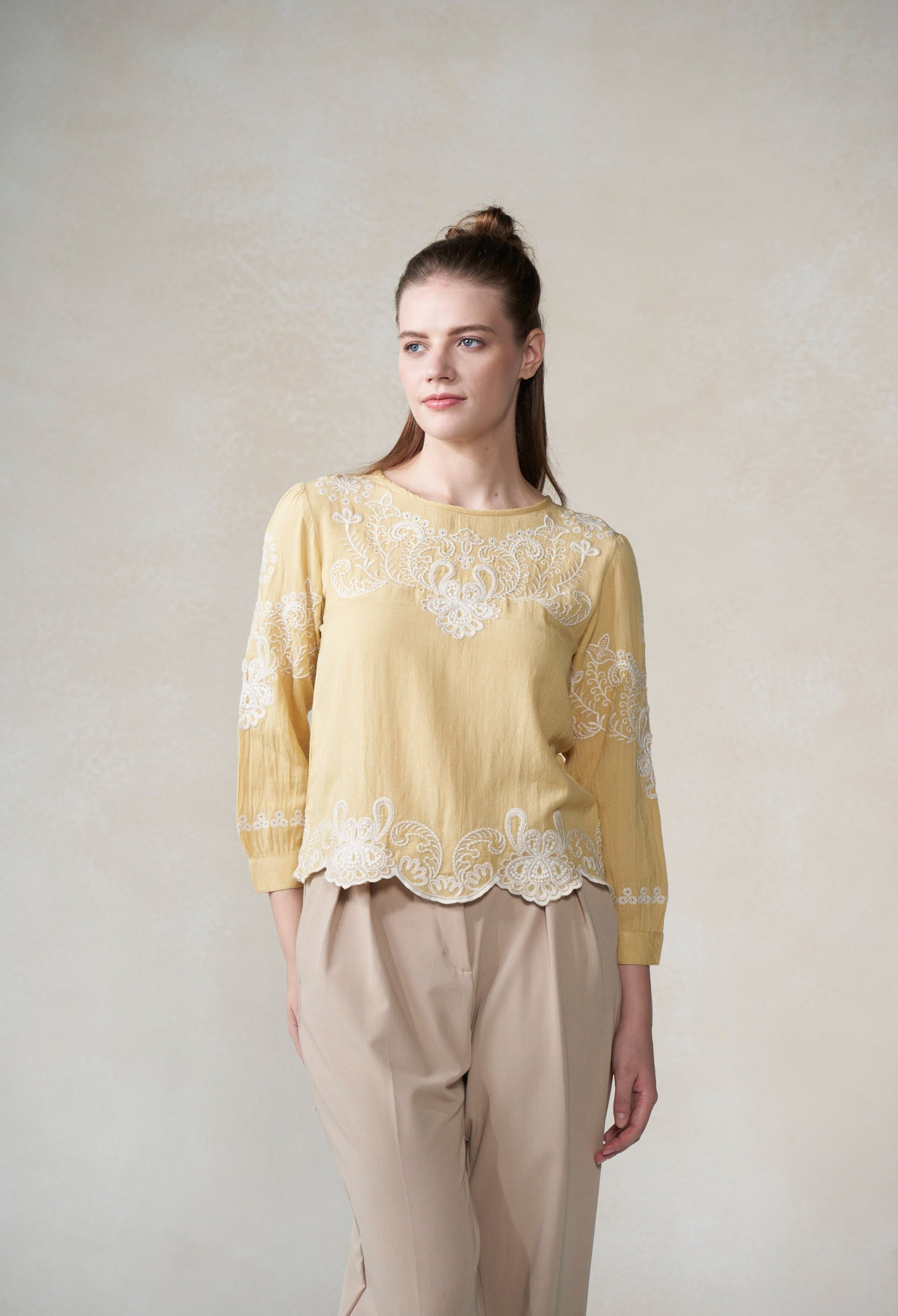 Woman wearing a yellow lace top and beige pants against a plain background