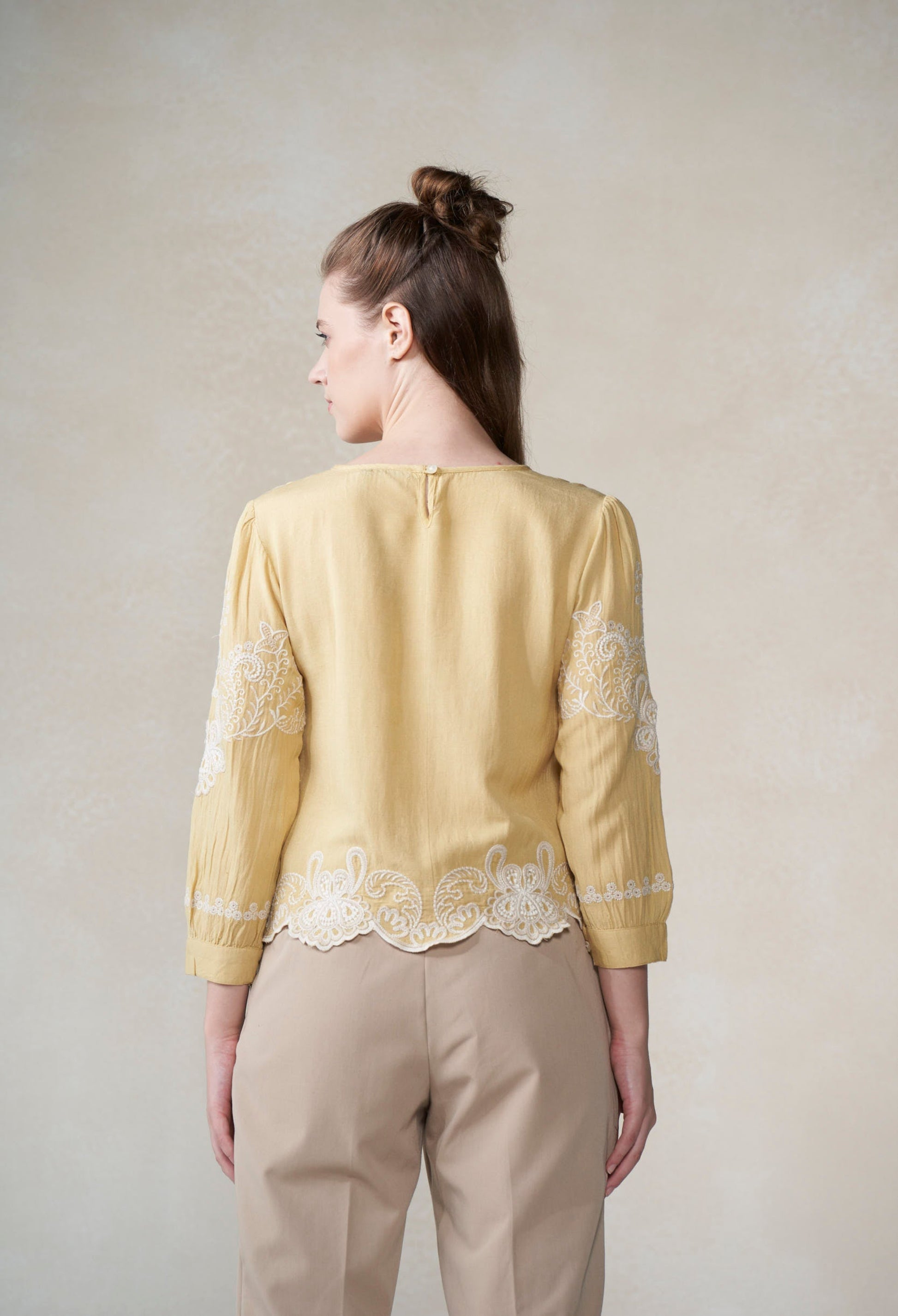 Woman wearing a yellow blouse with lace details on a plain background