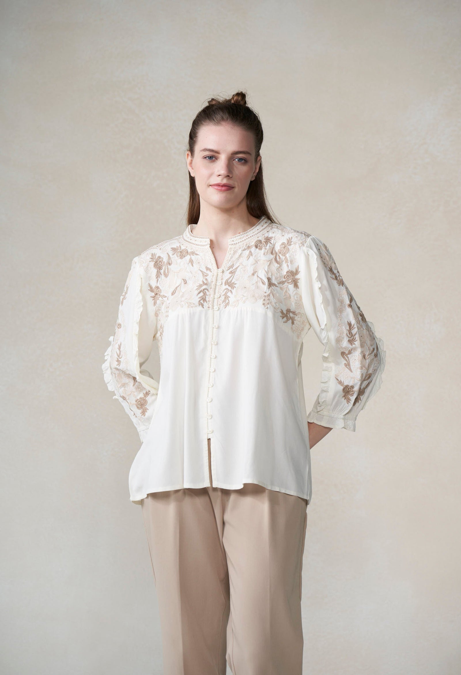 Woman wearing a white blouse with floral embroidery against a plain background