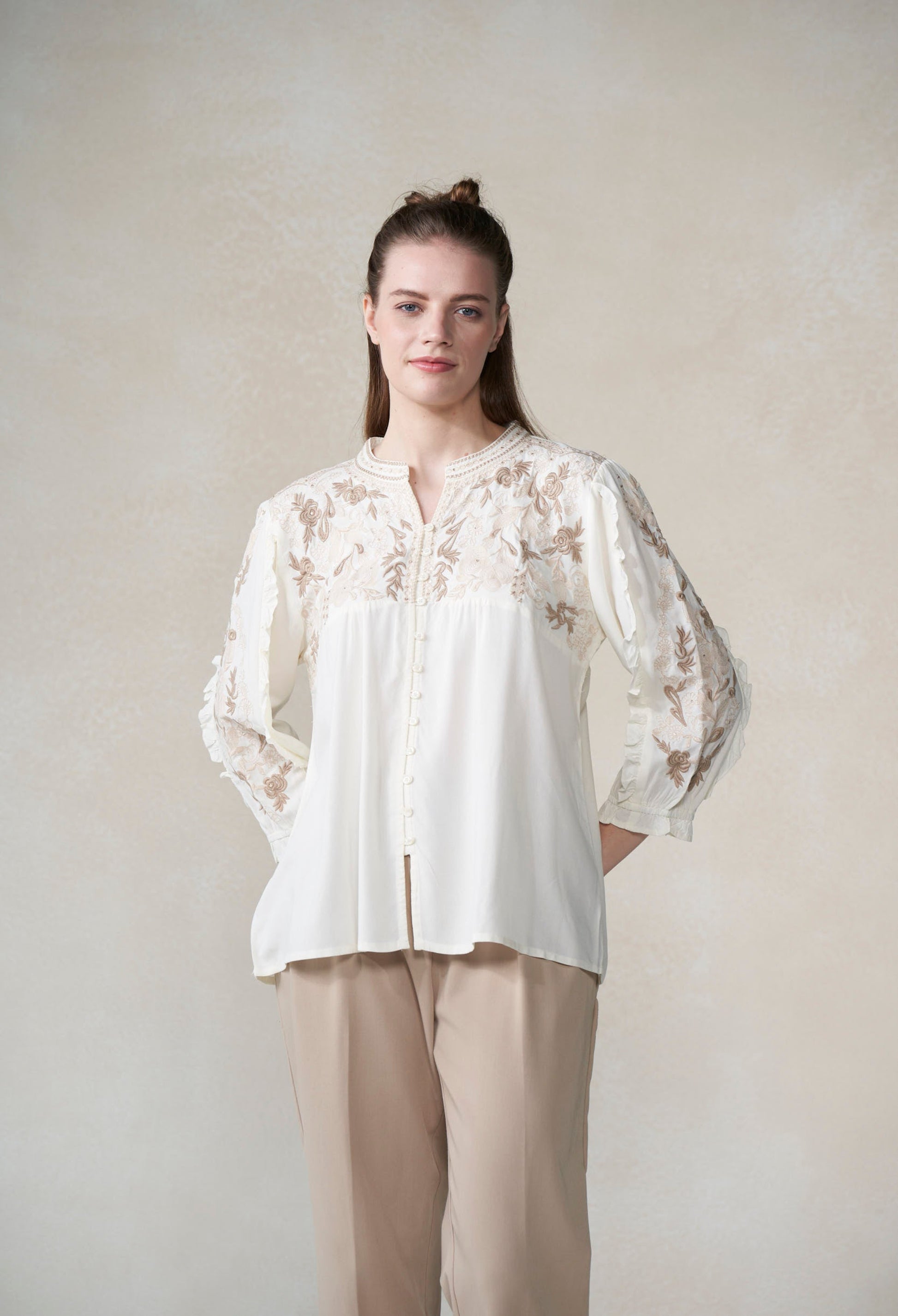 Woman wearing a white blouse with floral embroidery against a plain background