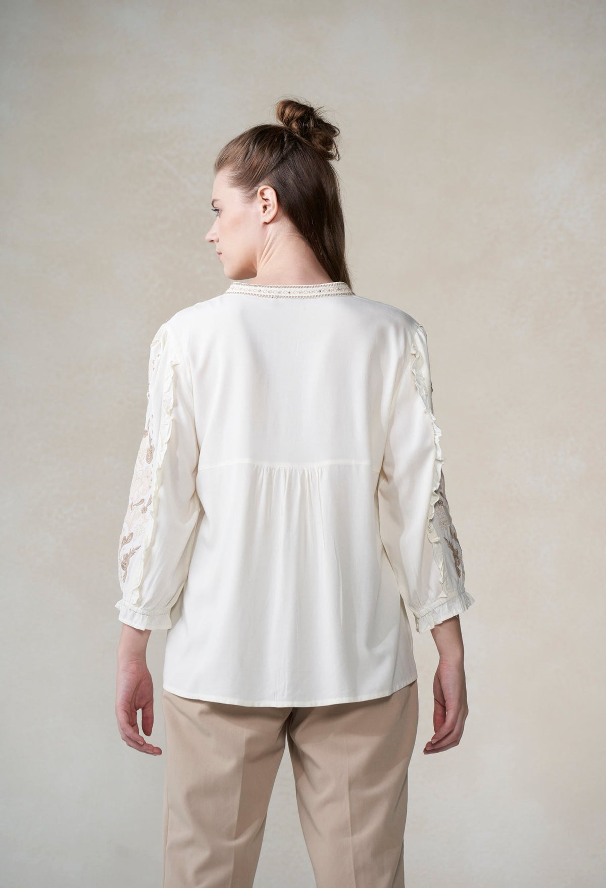 Woman wearing a white blouse with lace sleeves against a plain background