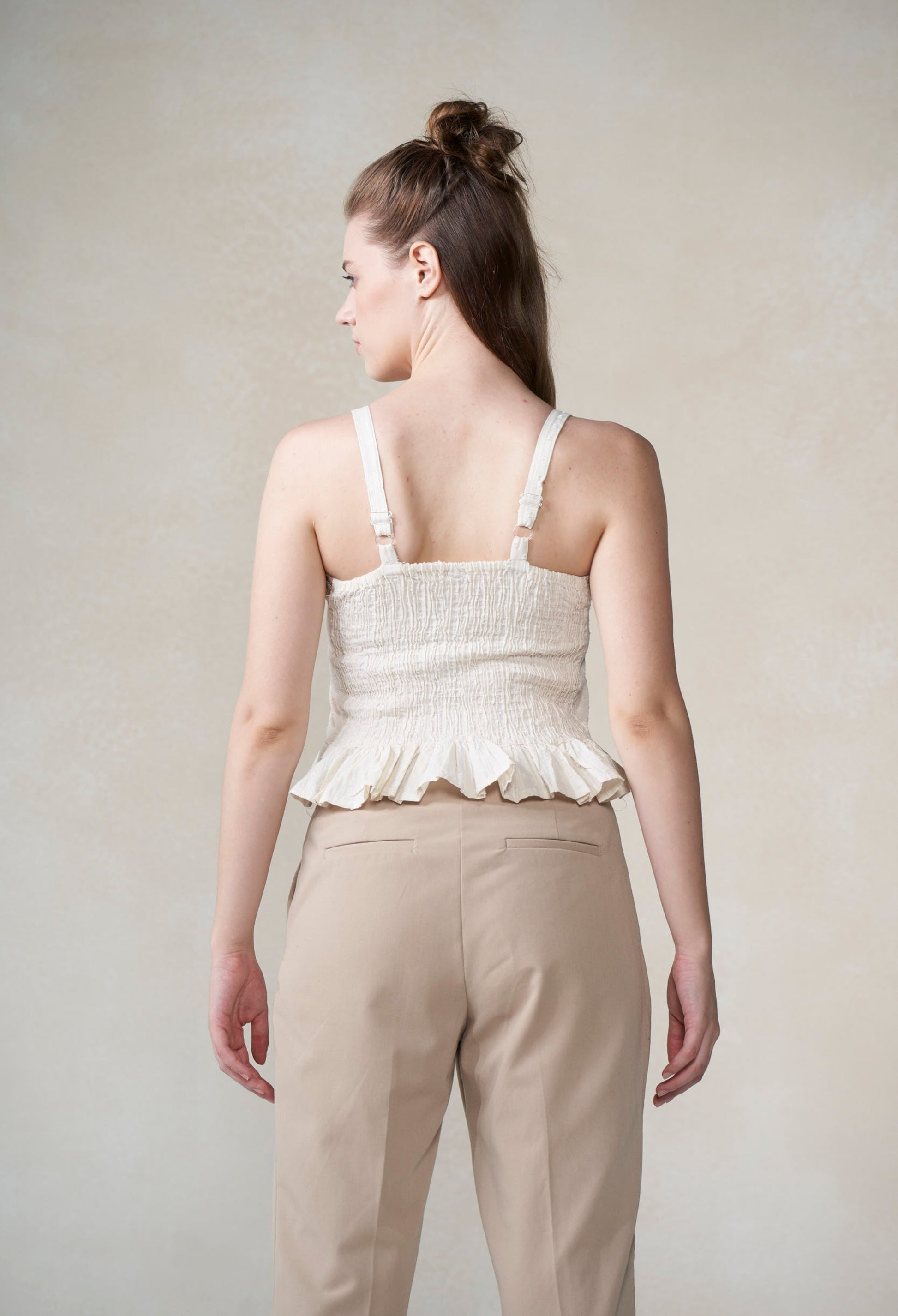 Woman wearing a white peplum top and beige pants against a plain background