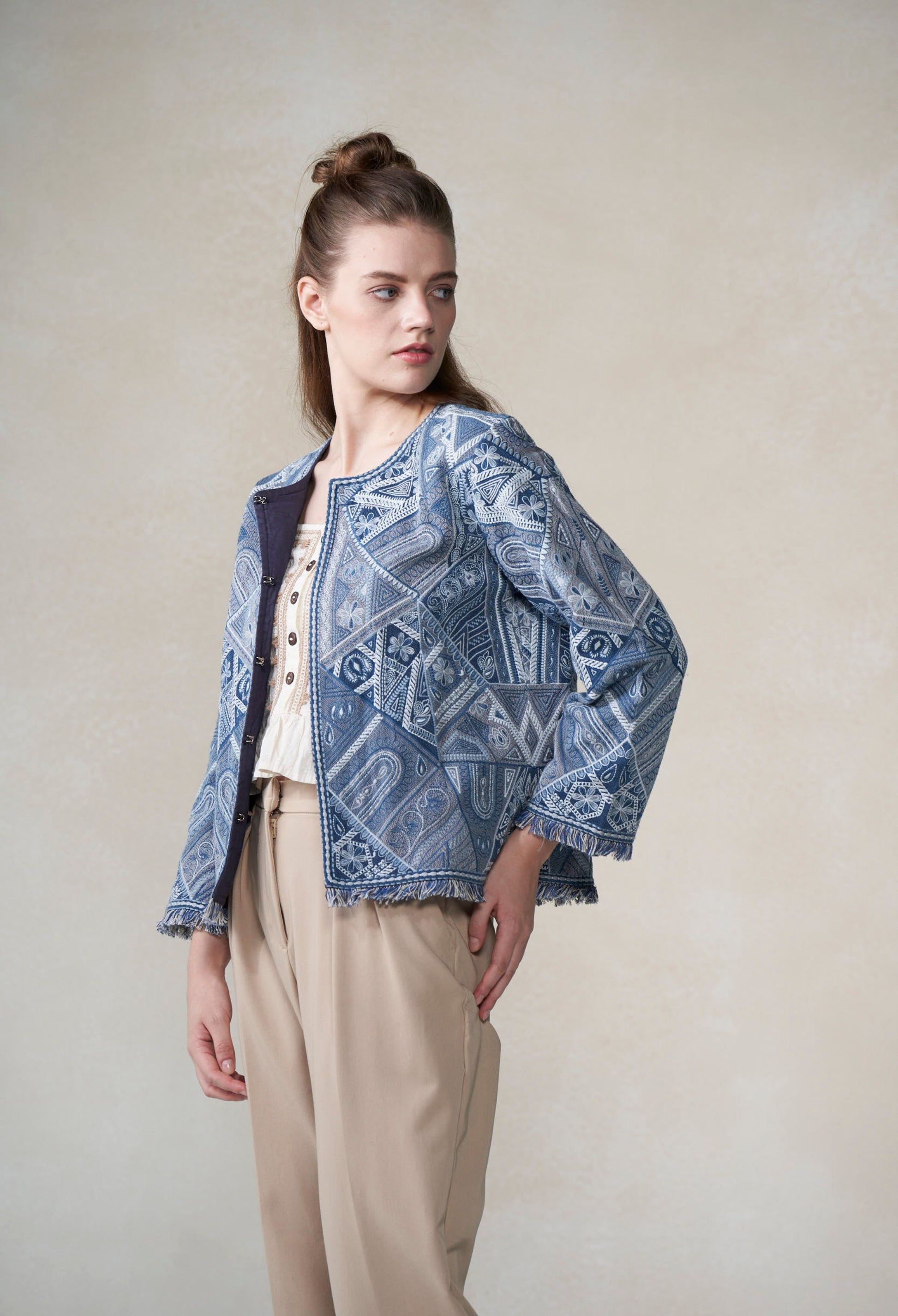 Woman wearing a blue patterned jacket over a white shirt and beige pants on a plain background