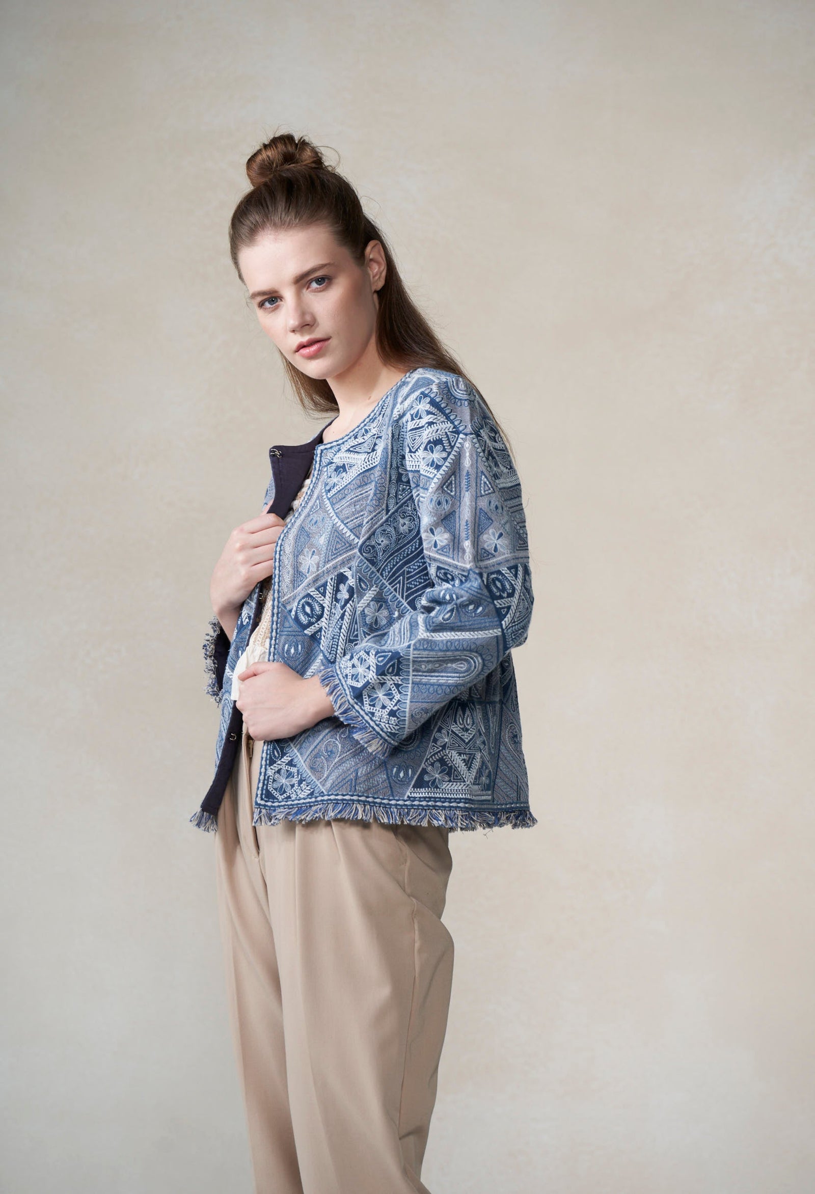 Woman wearing a patterned blue top and beige pants against a plain background