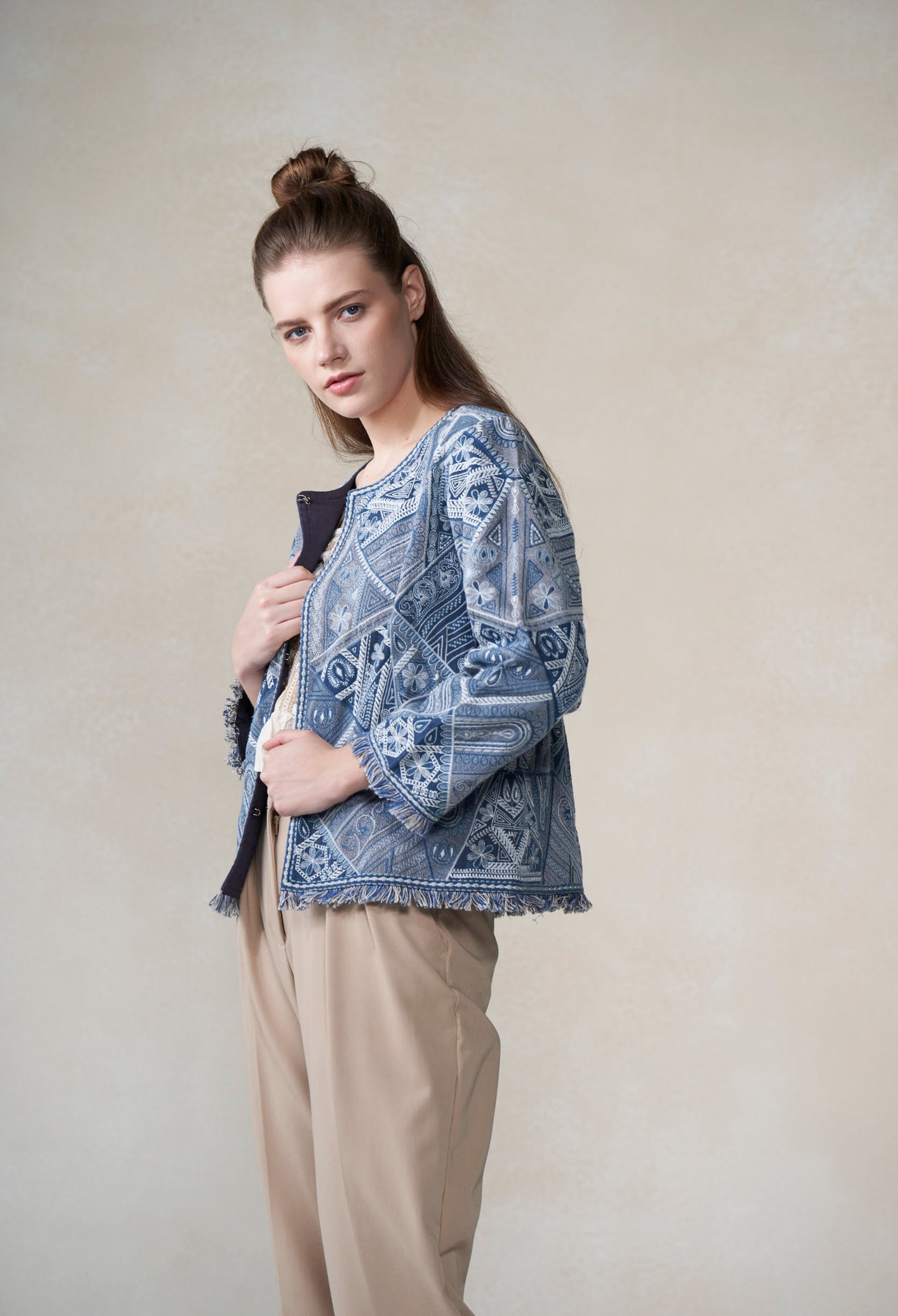 Woman wearing a patterned blue top and beige pants against a plain background