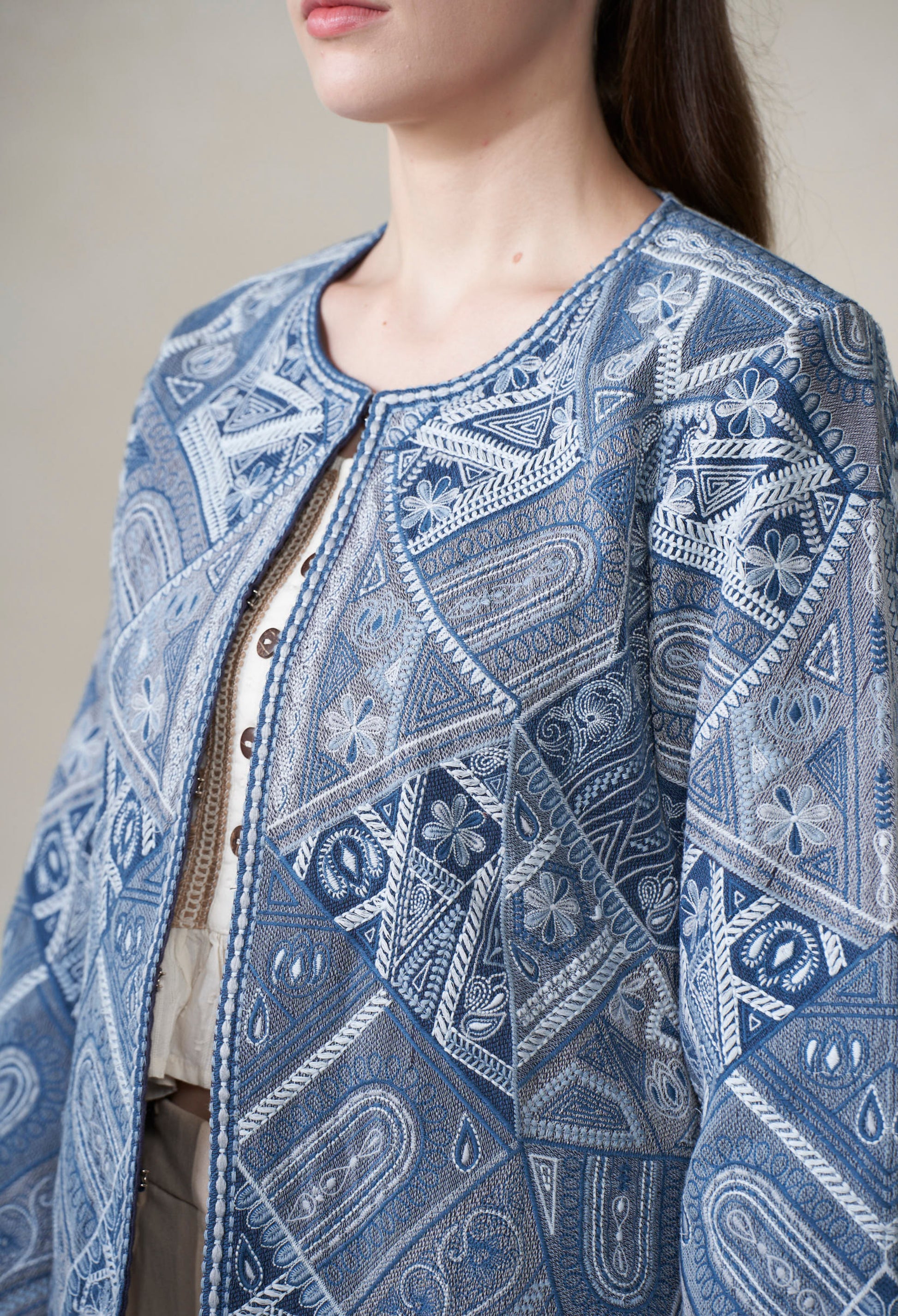 Close-up of a person wearing a blue patterned jacket  with white embroidery against a neutral background