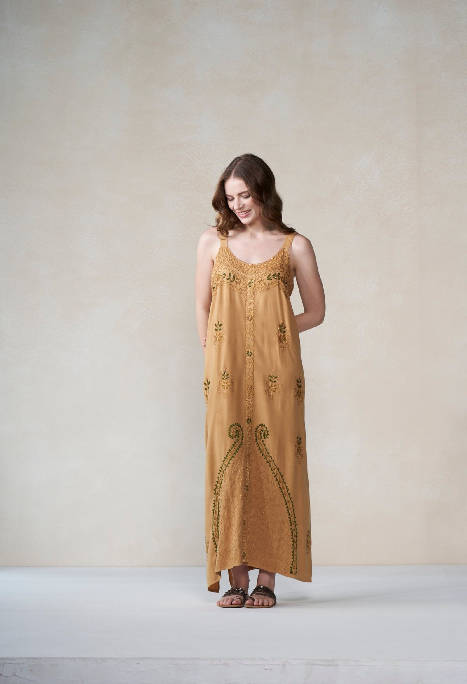 Woman wearing a long mustard yellow dress with intricate patterns against a plain background
