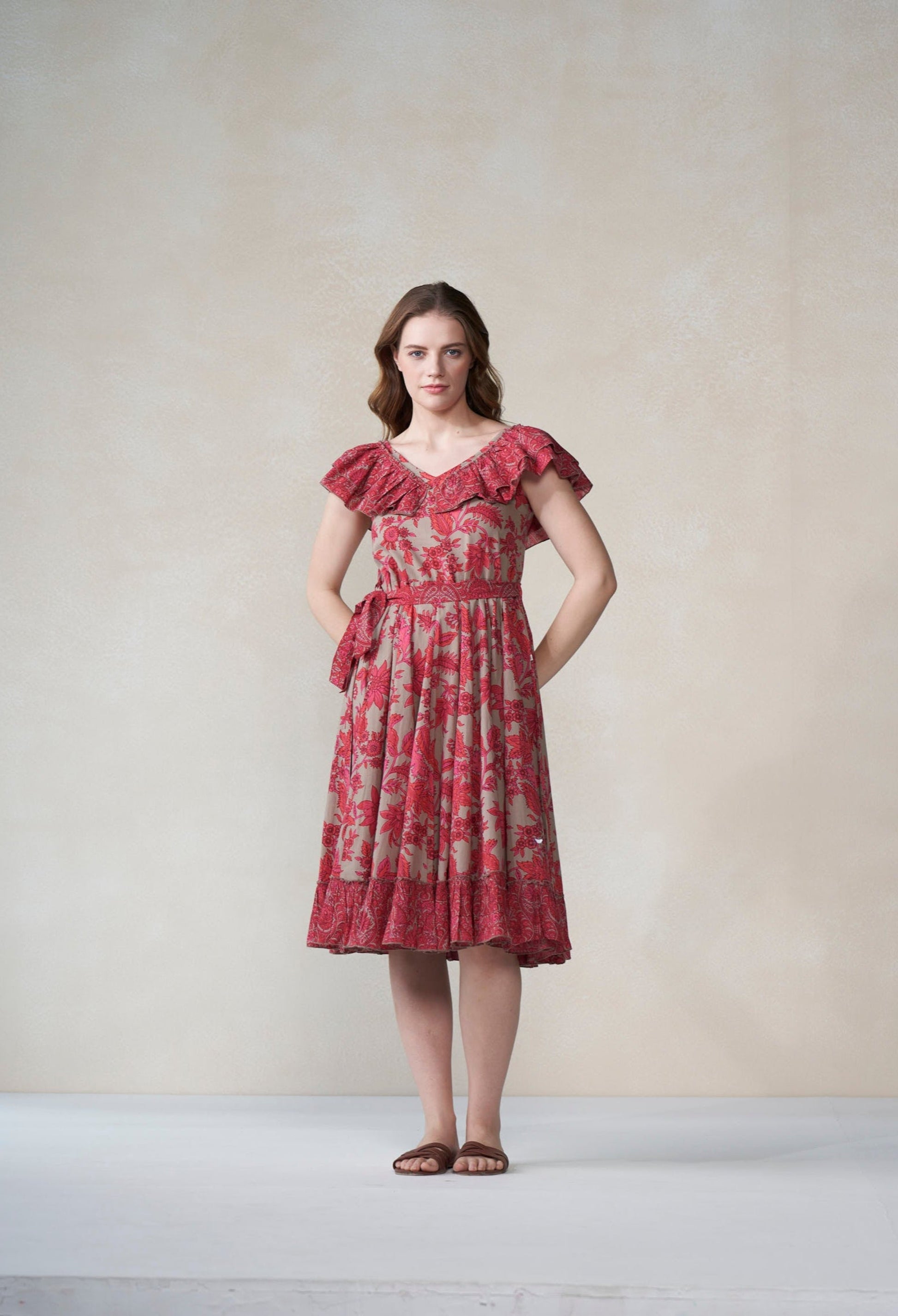 Woman wearing a red floral dress standing against a plain background