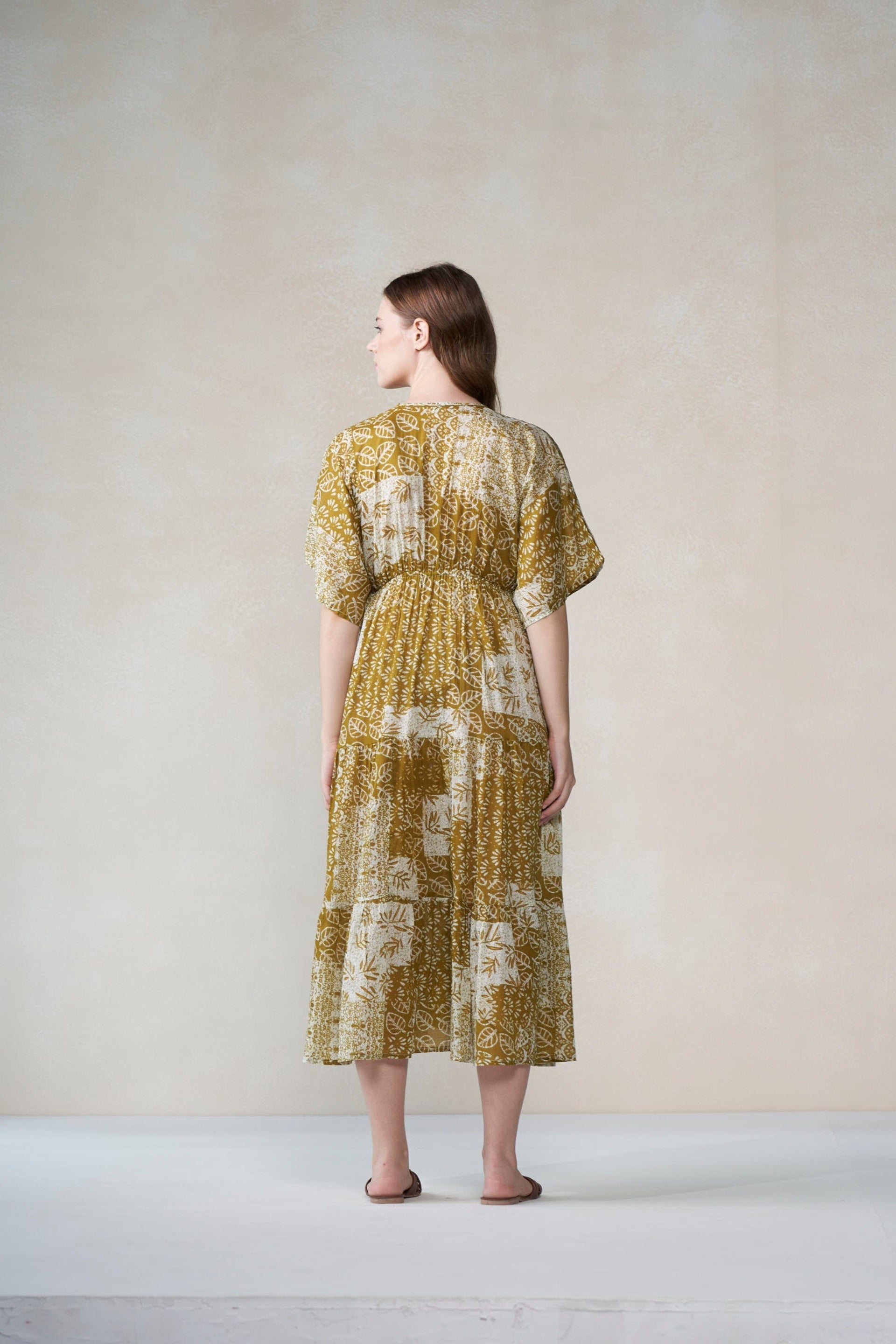 Woman wearing a mustard green floral dress against a plain background