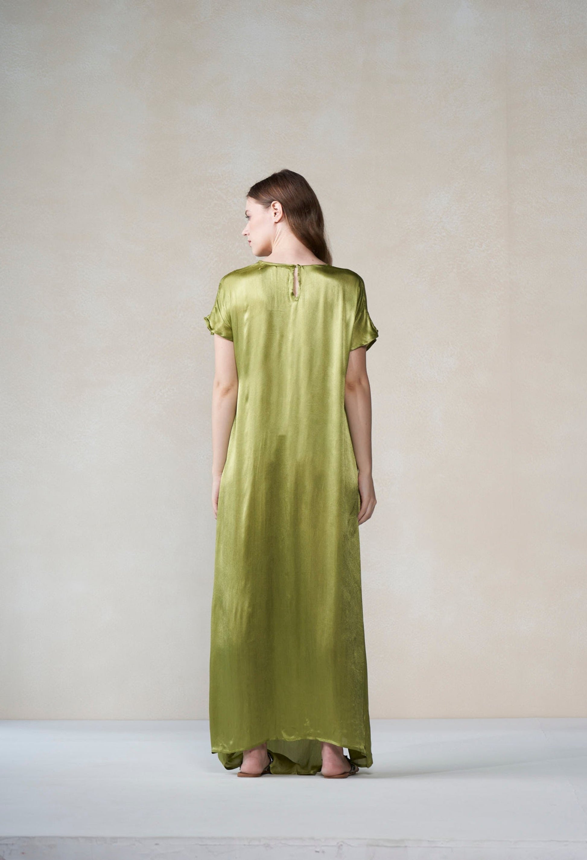 Woman wearing a long green dress standing against a plain background
