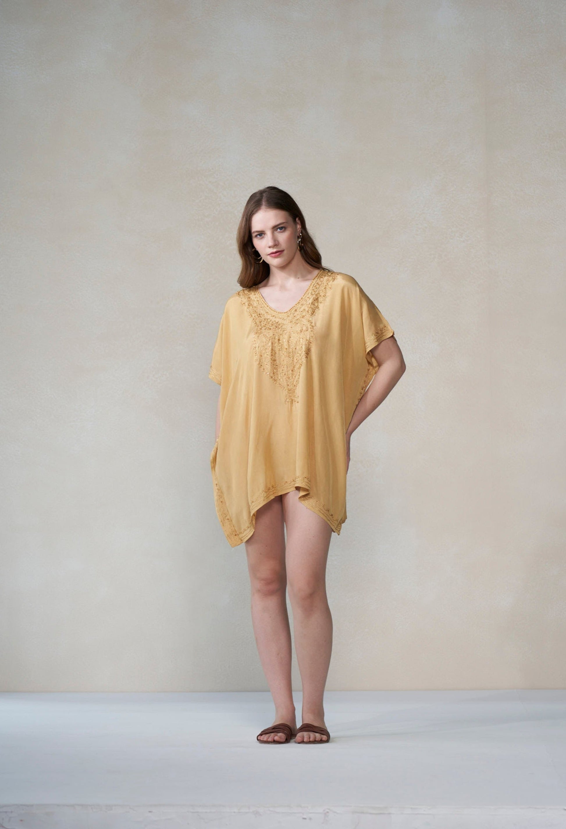 Woman wearing a mustard yellow kaftan against a plain background