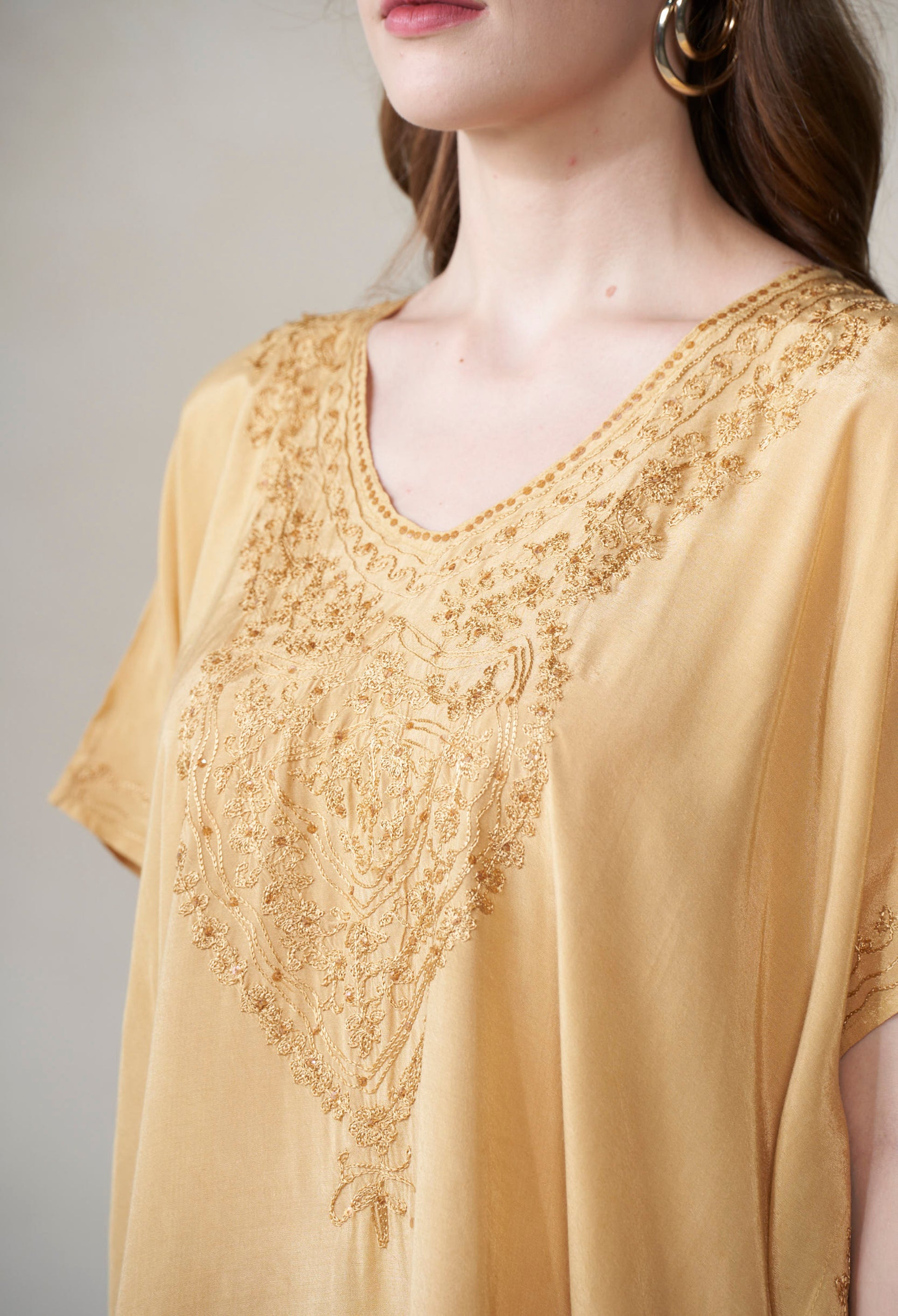 Close-up of a person wearing a mustard kaftan with intricate lace detailing on a plain background