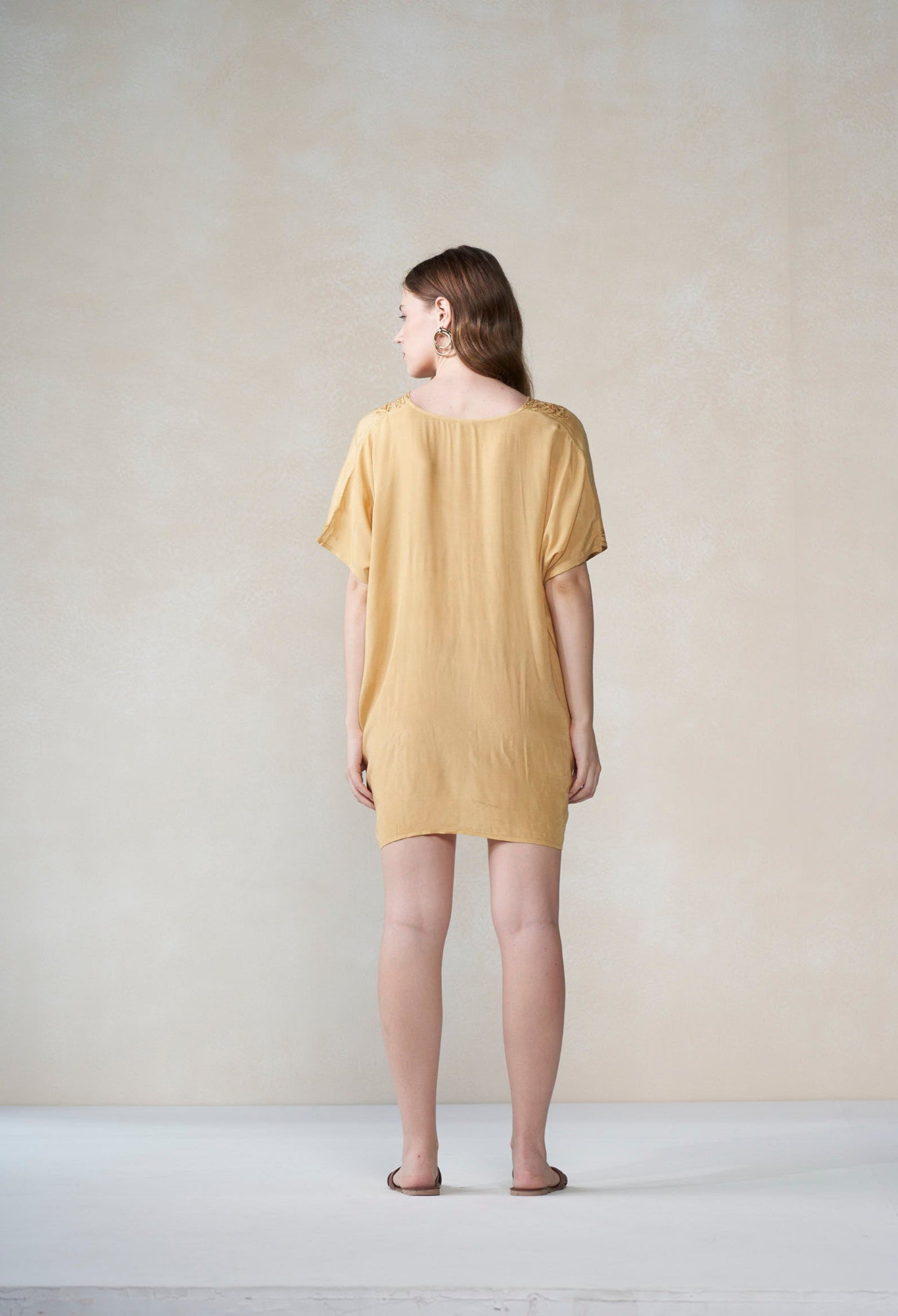 Woman wearing a mustard kaftan standing against a plain background