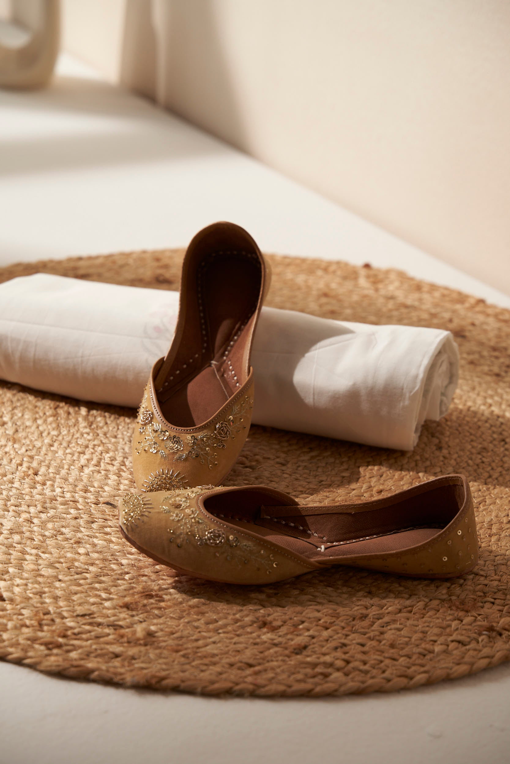 Pair of beautiful gold/mustard Indias juttis on a textured surface with decorative vases in the background