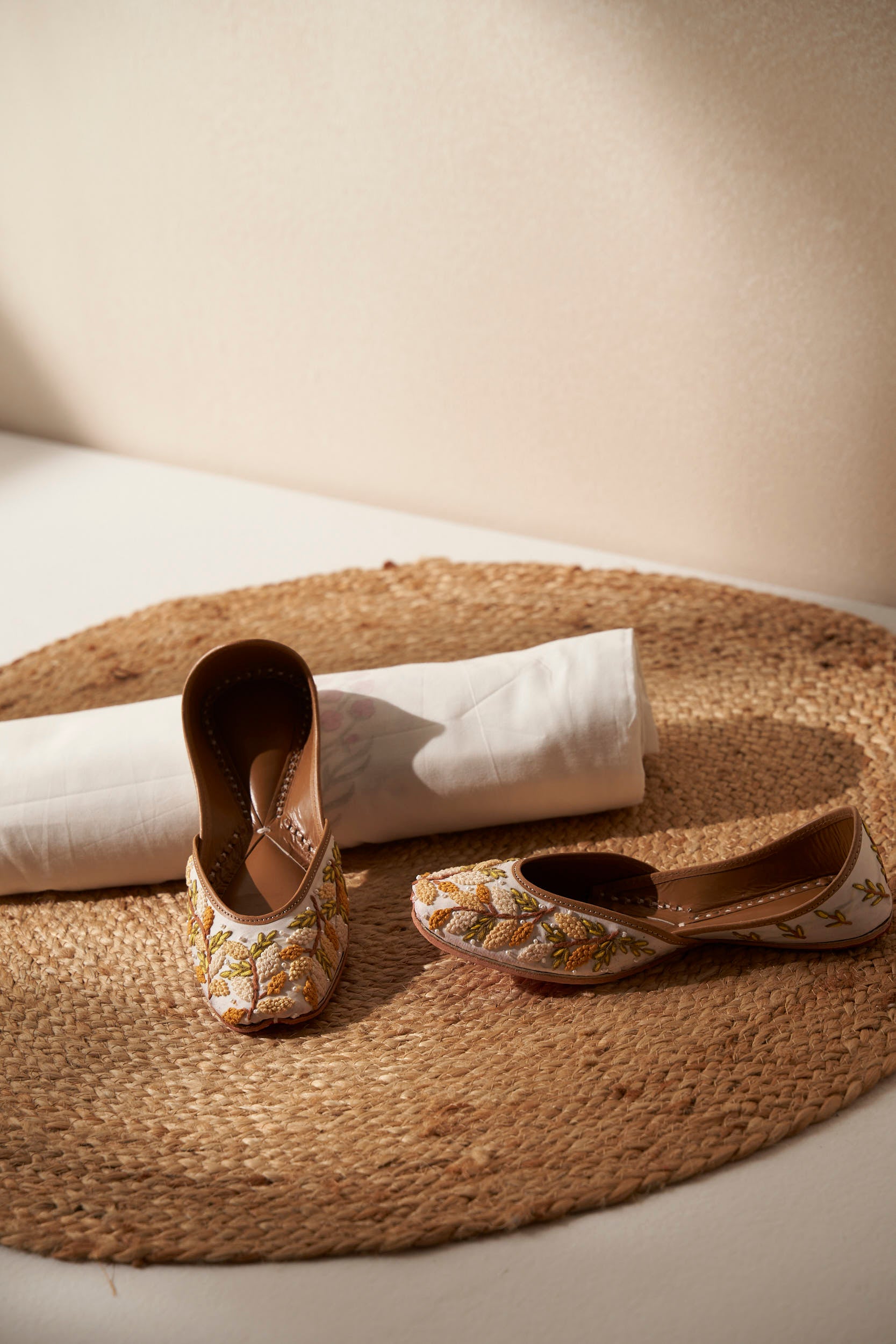 Pair of decorative white and yellow  royal indian shoes called juttis on a woven mat with a white dohar