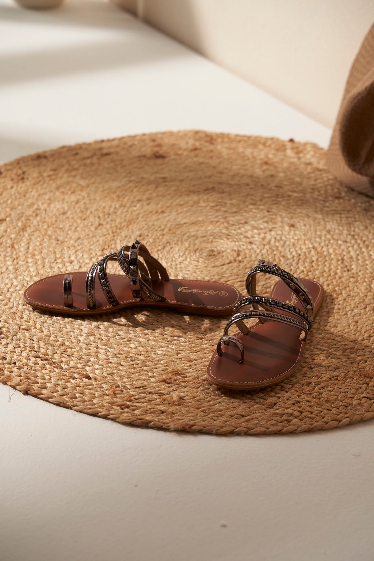 Pair of brown and silver sandals with decorative straps on a woven mat