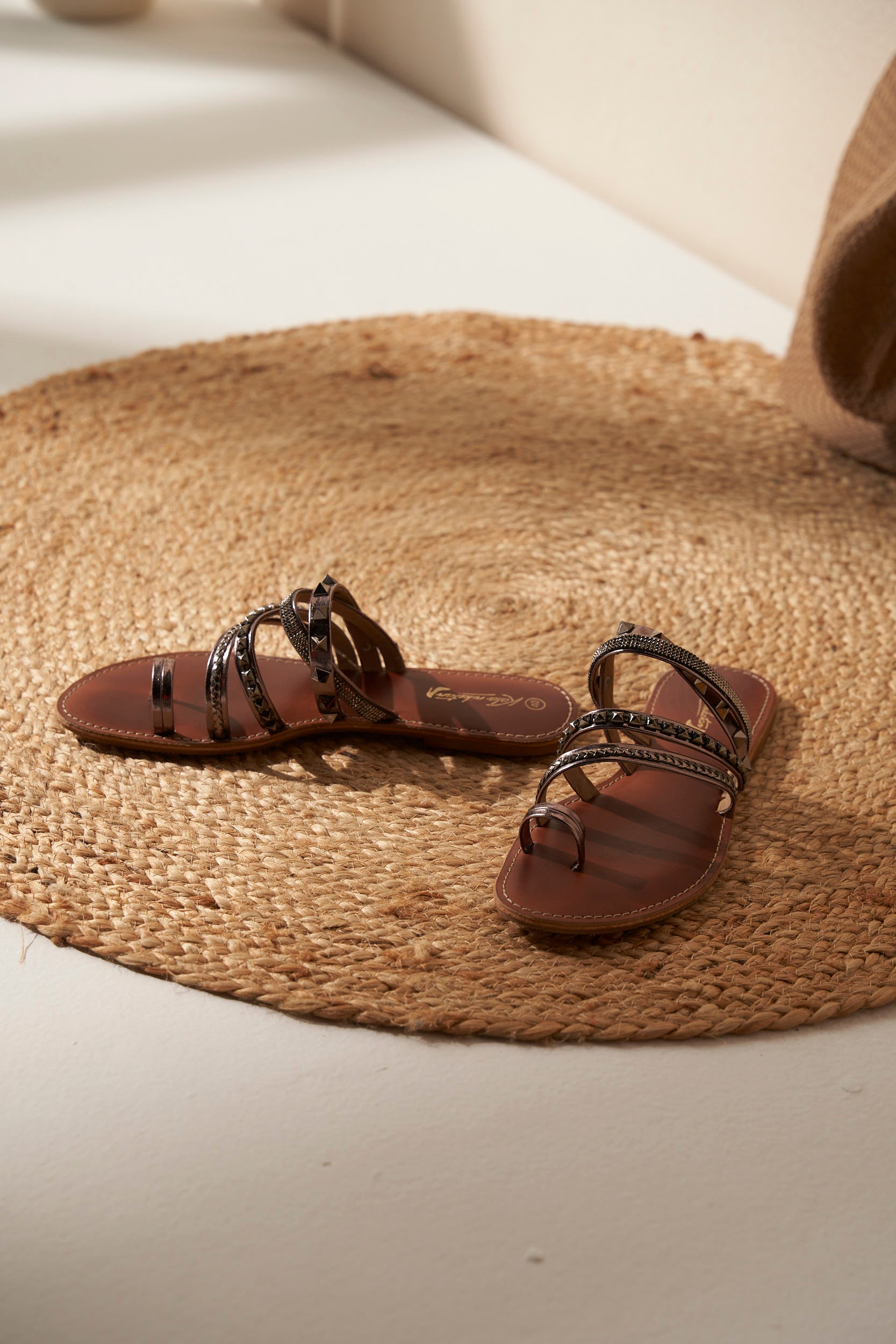 Pair of brown and silver sandals with decorative straps on a woven mat