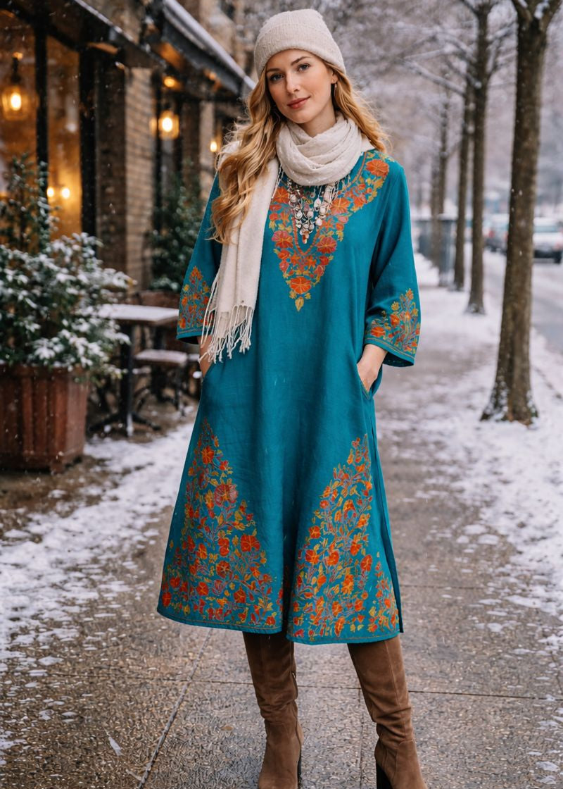 Woman in a teal dress with floral patterns walking on a snowy street.