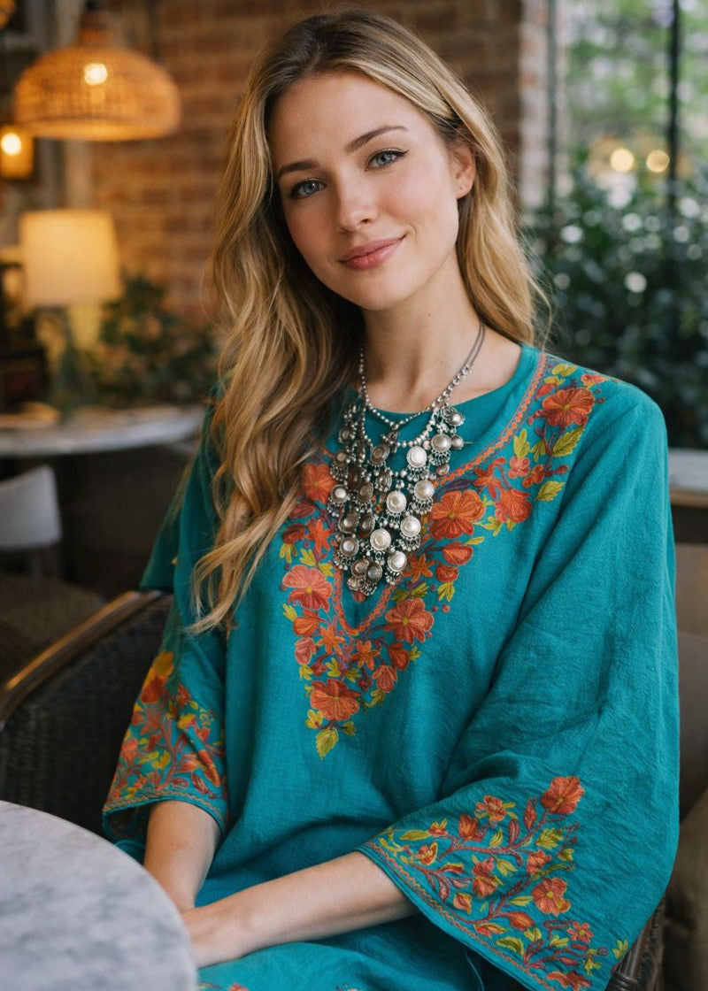 Woman wearing a teal embroidered dress with colorful patterns in an indoor setting.