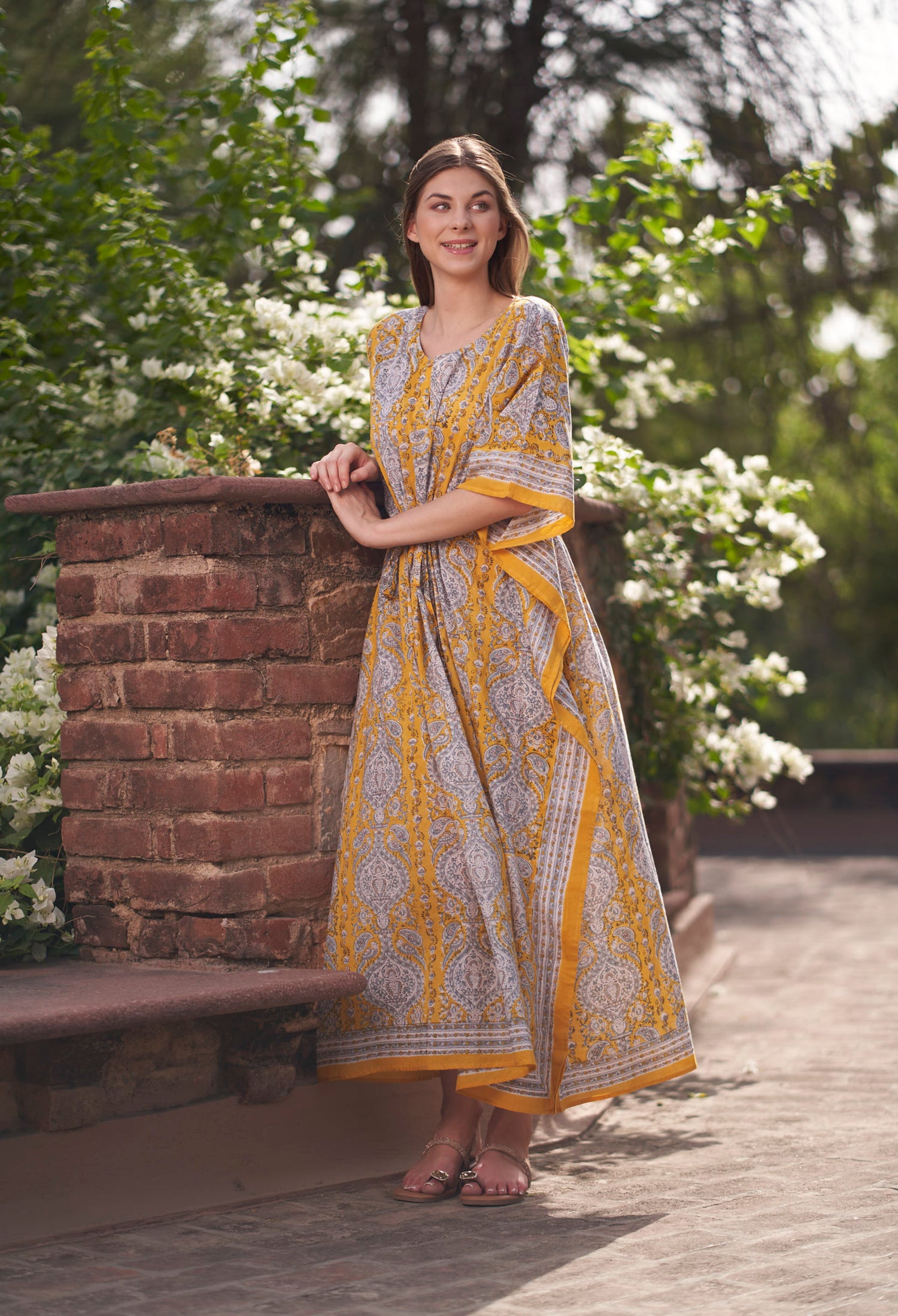 Woman in a yellow and white patterned dress standing outdoors with greenery in the background