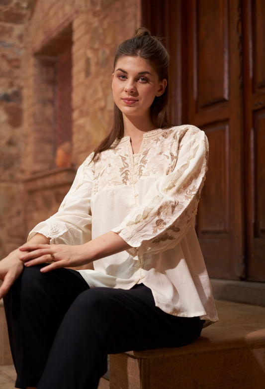 Woman wearing a white blouse sitting against a stone wall.